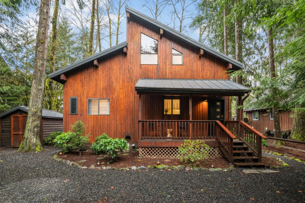 The inviting wooden facade of the retreat with a front porch nestled among towering trees. The setting is welcoming, blending the home seamlessly into its forested surroundings and inviting guests to enjoy peaceful mornings or relaxing evenings on the porch.