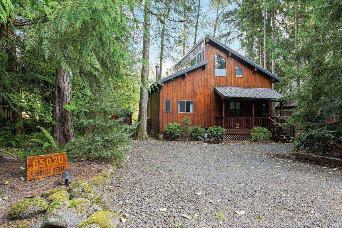 The photo captures a wooden cabin surrounded by tranquil trees, a gravel driveway, and a welcoming porch. The natural landscaping and open yard evoke the peaceful, dog-friendly atmosphere described in the section.
