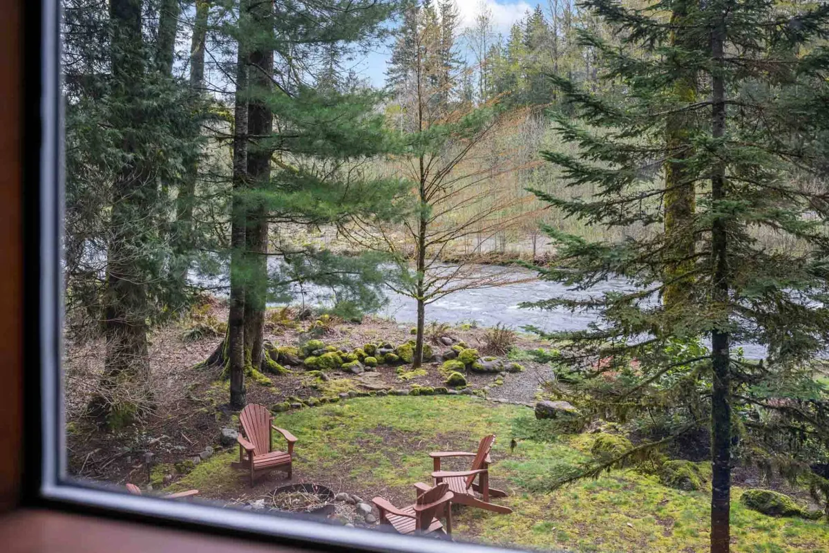 This image shows a peaceful riverside setting with adirondack chairs facing the river, surrounded by moss-covered stones and lush trees. The scene is ideal for relaxation, family gatherings, and observing wildlife along the riverbank.