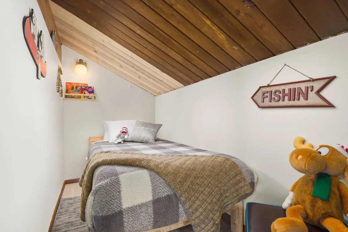 A playful and inviting bedroom scene with a wooden ceiling, plush toys, a fishing-themed sign, and cozy bed linens. The space feels whimsical and ideal for children, emphasizing comfort and creativity.