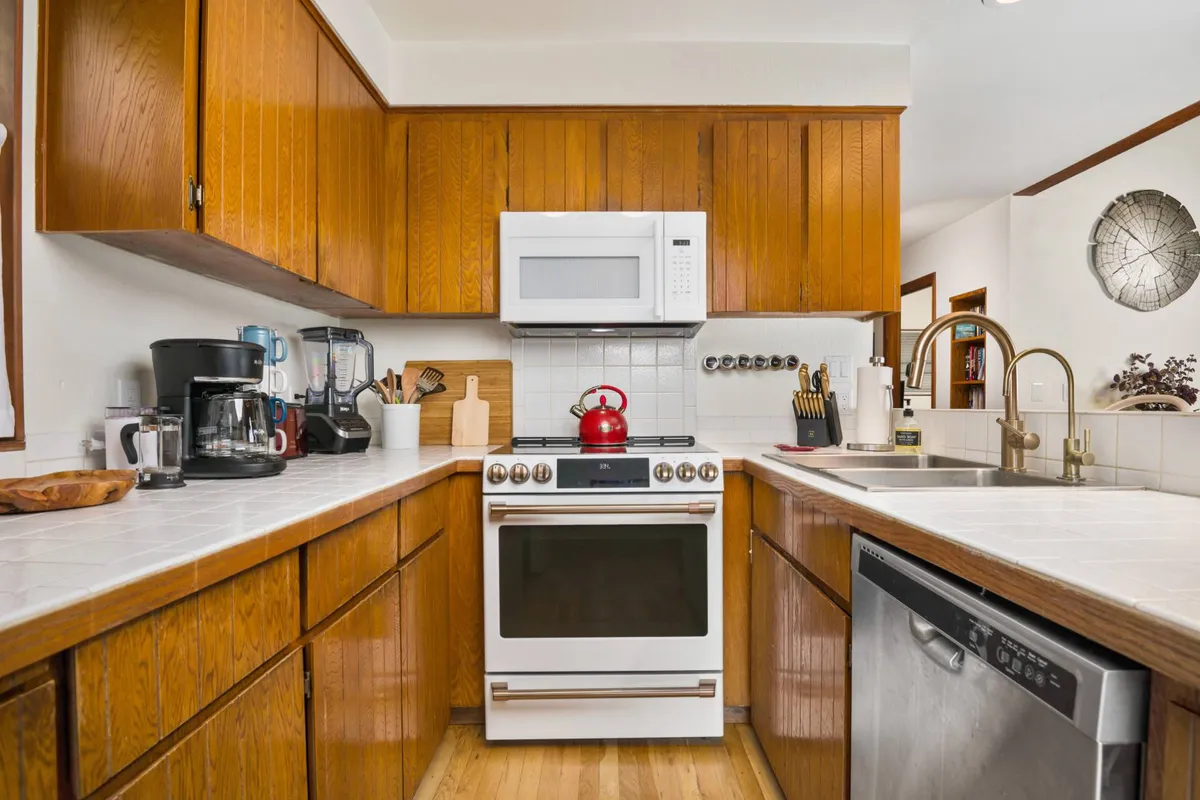 A homey kitchen scene with a classic stove, bright red kettle, deep kitchen sink, and rich wooden cabinetry. The space feels both modern and welcoming, suitable for preparing anything from hearty family dinners to quick snacks.