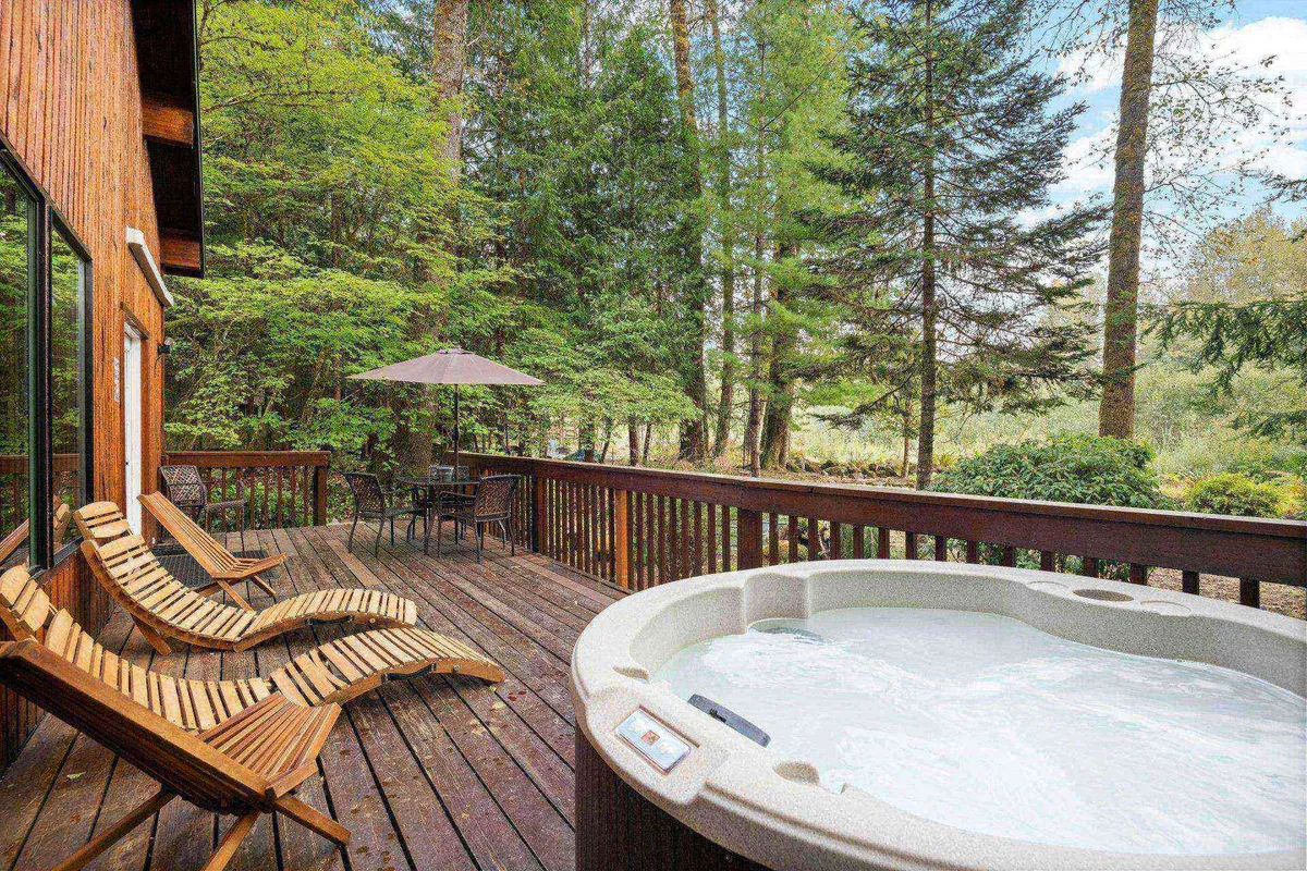 The photo showcases a large, inviting deck featuring a hot tub, deck chairs, dining table, and views of surrounding trees. The setup encourages outdoor socializing, dining al fresco, and relaxing in nature. The harmonious integration of amenities supports both cozy couple time and lively group gatherings.
