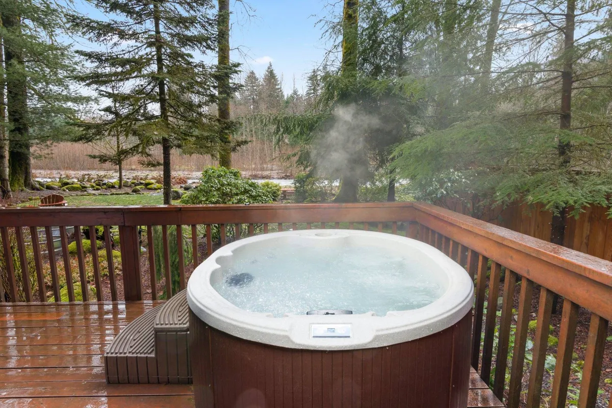 This image features a serene outdoor hot tub set on a deck surrounded by lush trees, creating a private and tranquil retreat. The positioning of the hot tub allows for expansive views of the natural surroundings, ideal for soaking in the ambiance and unwinding. The deck area is spacious enough to accommodate socializing and relaxing with loved ones.